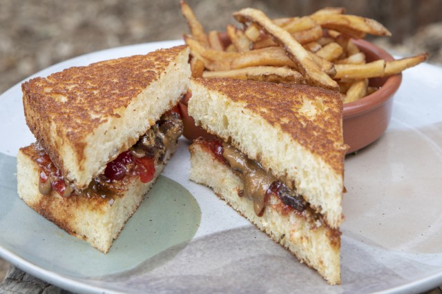 Sandwich of housemade sunbutter and grape jelly on toasted brioche on a plate with french fries